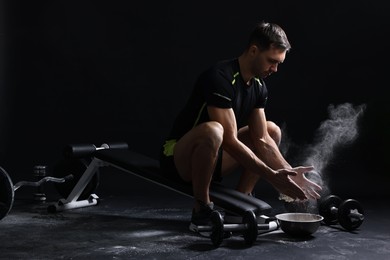 Man clapping hands with talcum powder before training on black background