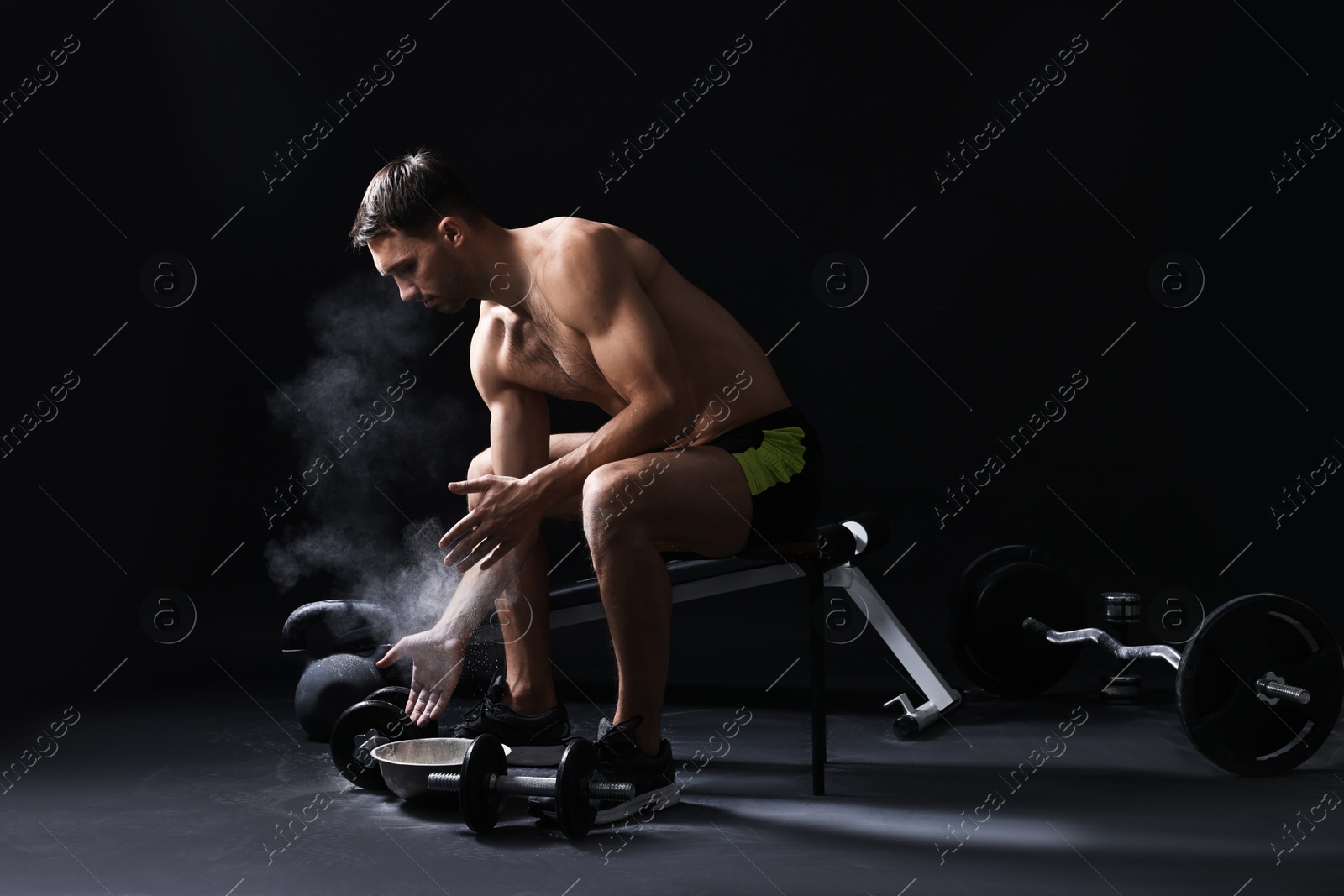 Photo of Man applying talcum powder onto his hands before training on black background