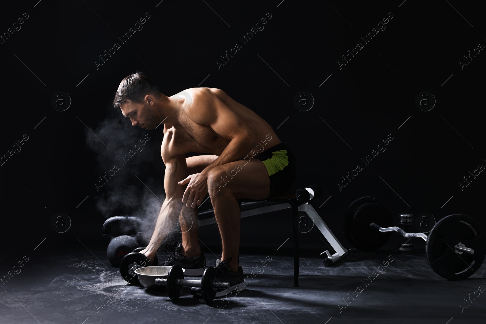 Photo of Man with talcum powder on hands training with barbell against black background