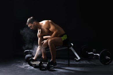 Photo of Man with talcum powder on hands training with barbell against black background