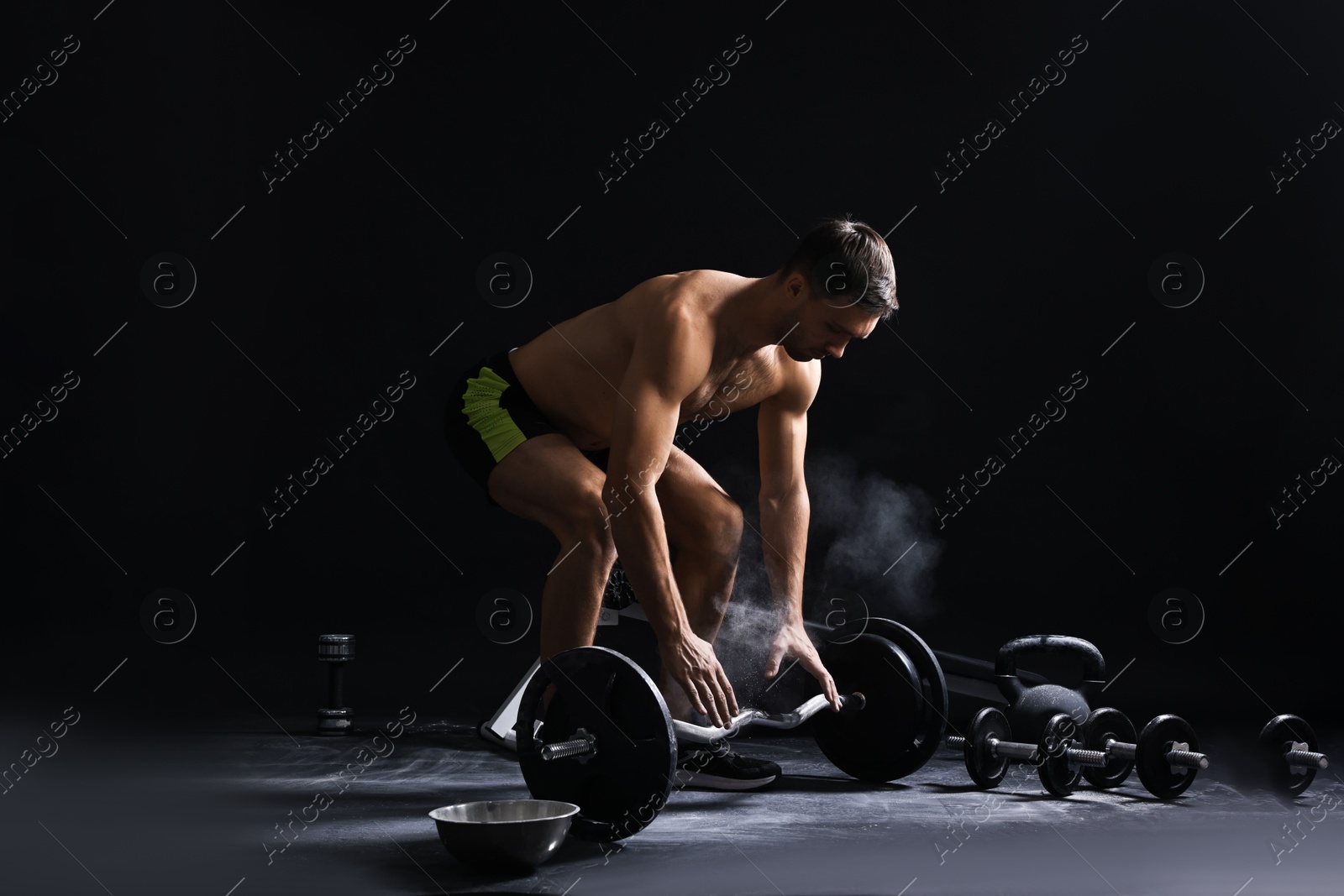 Photo of Man with talcum powder on hands training with barbell against black background