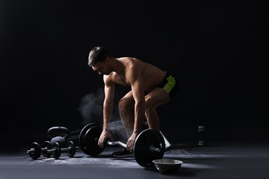 Man with talcum powder on hands training with barbell against black background