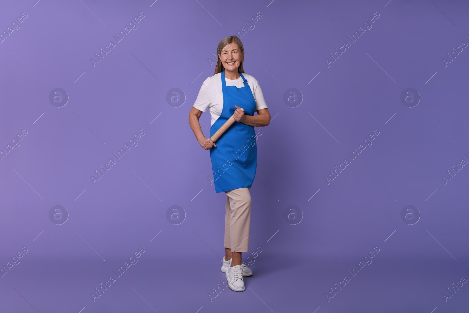 Photo of Happy woman with rolling pin on violet background