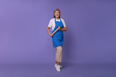 Happy woman with rolling pin on violet background