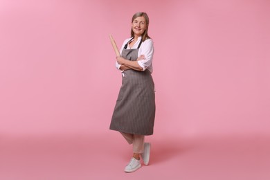 Happy woman with rolling pin on pink background