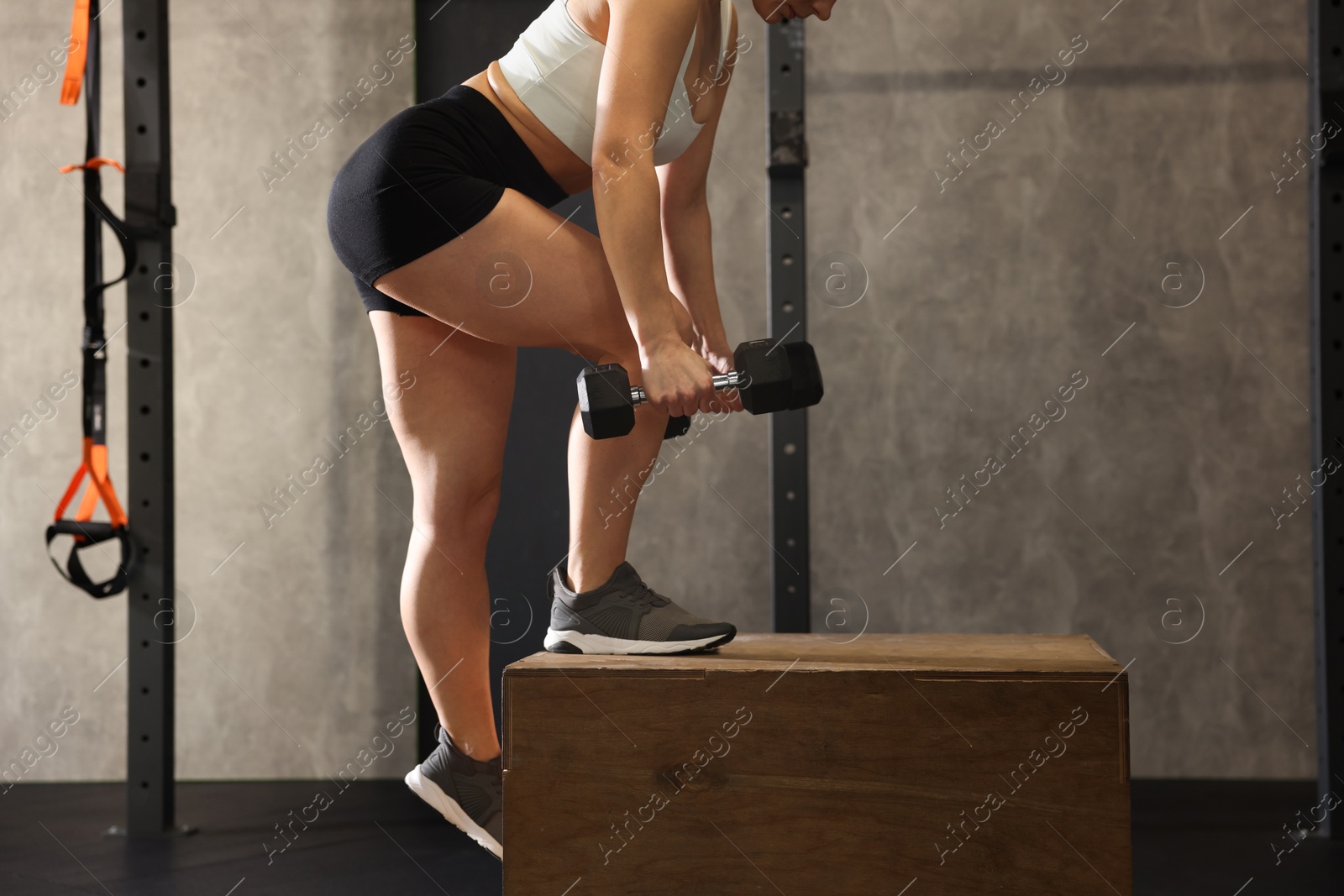 Photo of Sportswoman with dumbbells exercising on cube during crossfit workout in gym