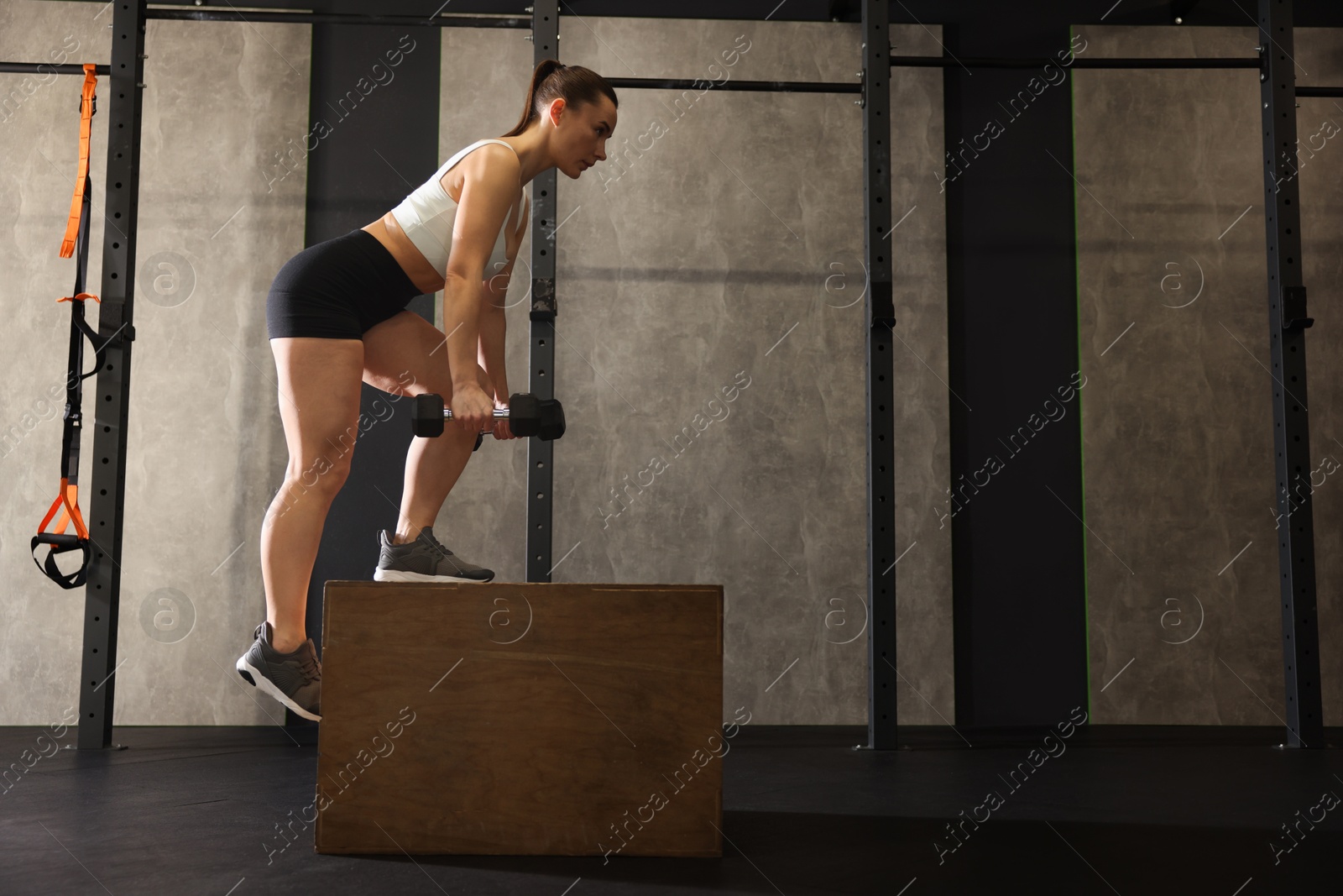 Photo of Sportswoman with dumbbells exercising on cube during crossfit workout in gym. Space for text