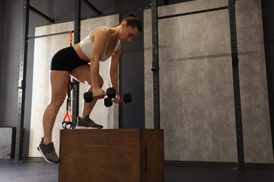 Sportswoman with dumbbells exercising on cube during crossfit workout in gym. Space for text