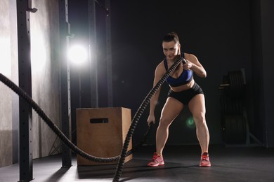 Sportswoman exercising with battle ropes during crossfit workout in gym