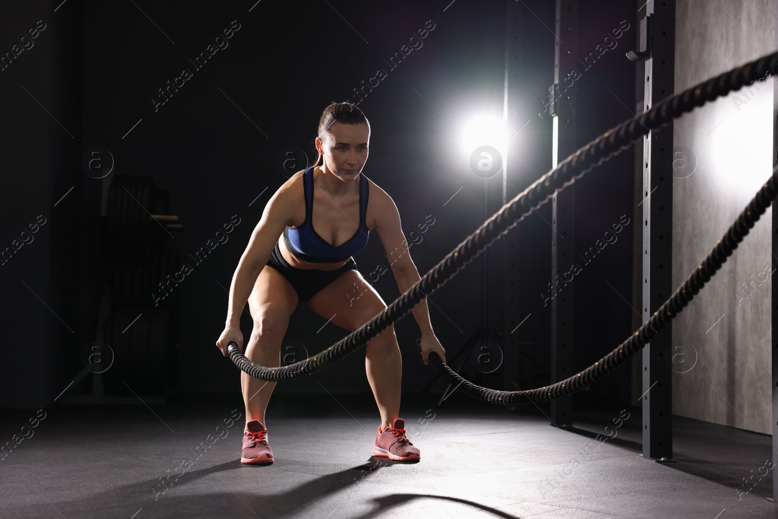 Photo of Sportswoman exercising with battle ropes during crossfit workout in gym