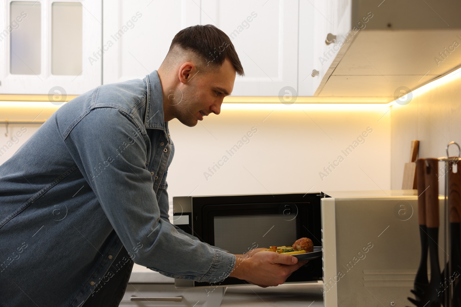 Photo of Man putting plate with lunch into microwave in kitchen