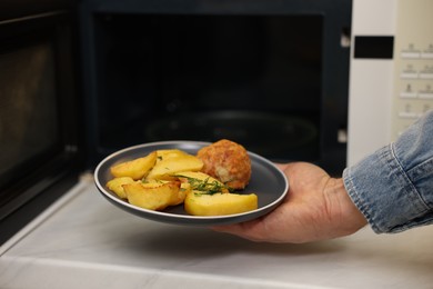 Photo of Man putting plate with lunch into microwave in kitchen, closeup