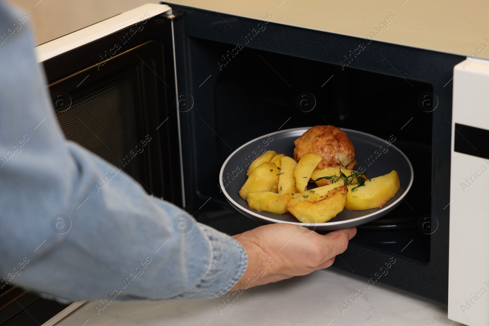 Photo of Man putting plate with lunch into microwave in kitchen, closeup