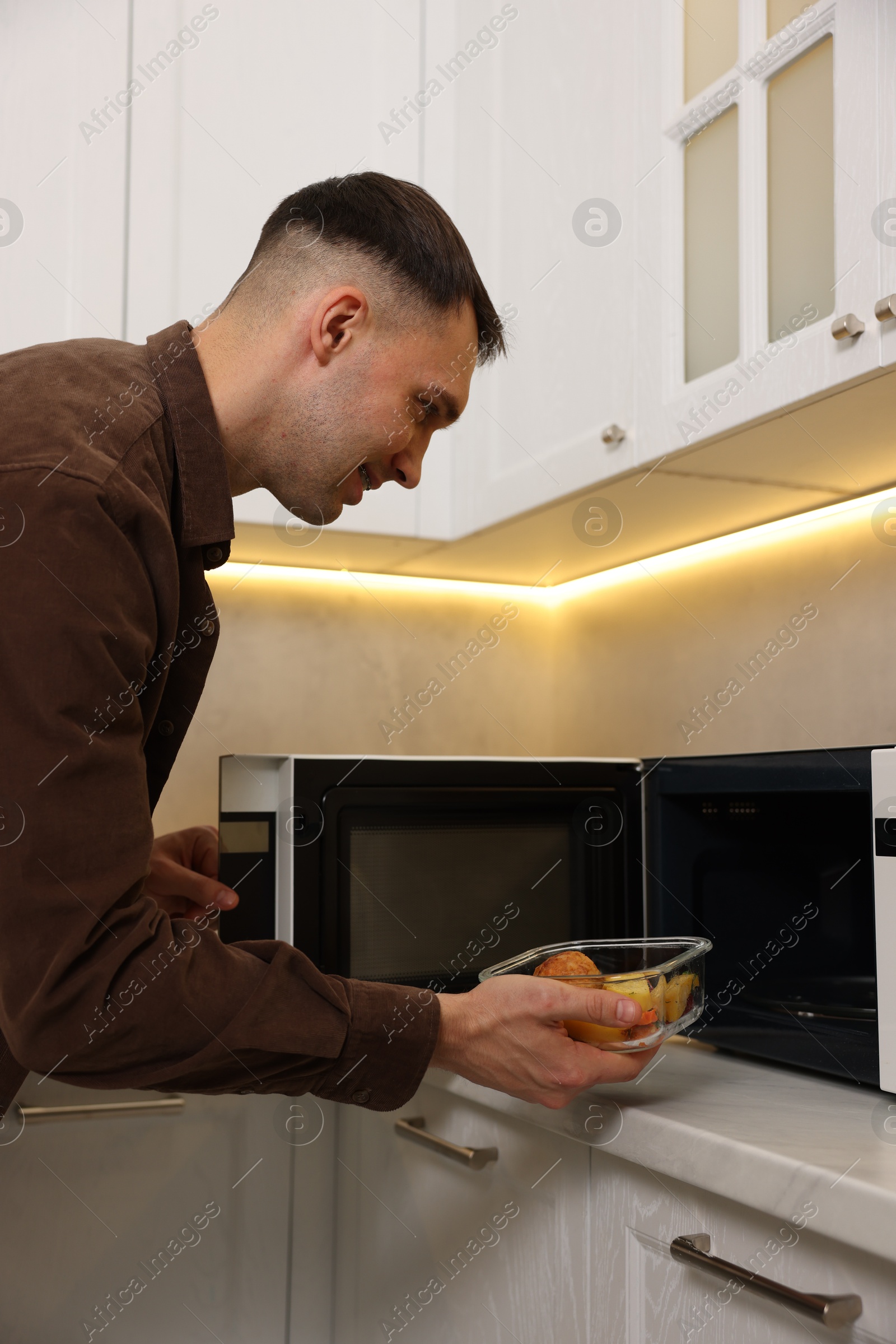 Photo of Man putting container with lunch into microwave in kitchen