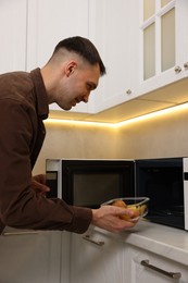 Photo of Man putting container with lunch into microwave in kitchen