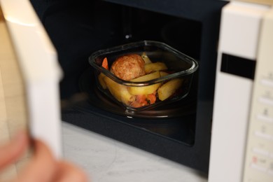 Photo of Man putting container with lunch into microwave in kitchen, closeup