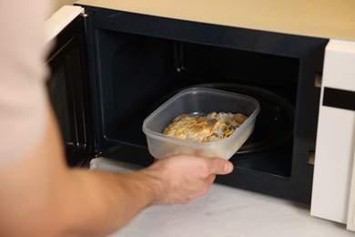 Photo of Man putting container with lunch into microwave in kitchen, closeup