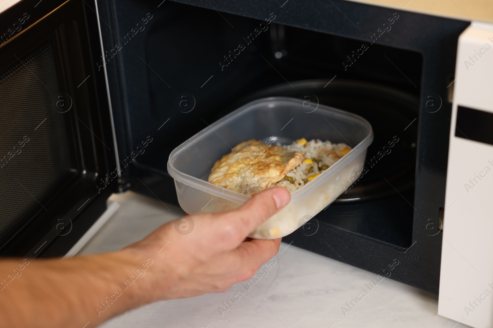 Photo of Man putting container with lunch into microwave in kitchen, closeup