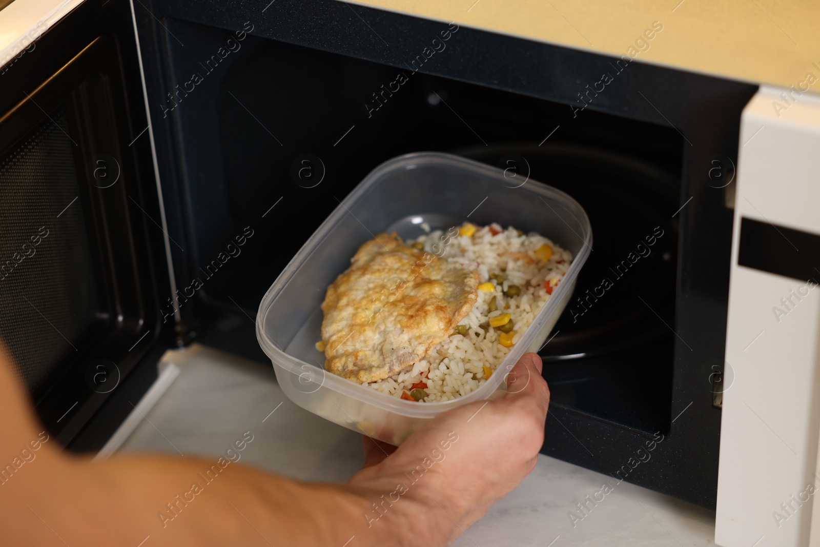 Photo of Man putting container with lunch into microwave in kitchen, closeup