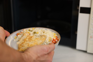 Photo of Man putting plate with lunch into microwave in kitchen, closeup