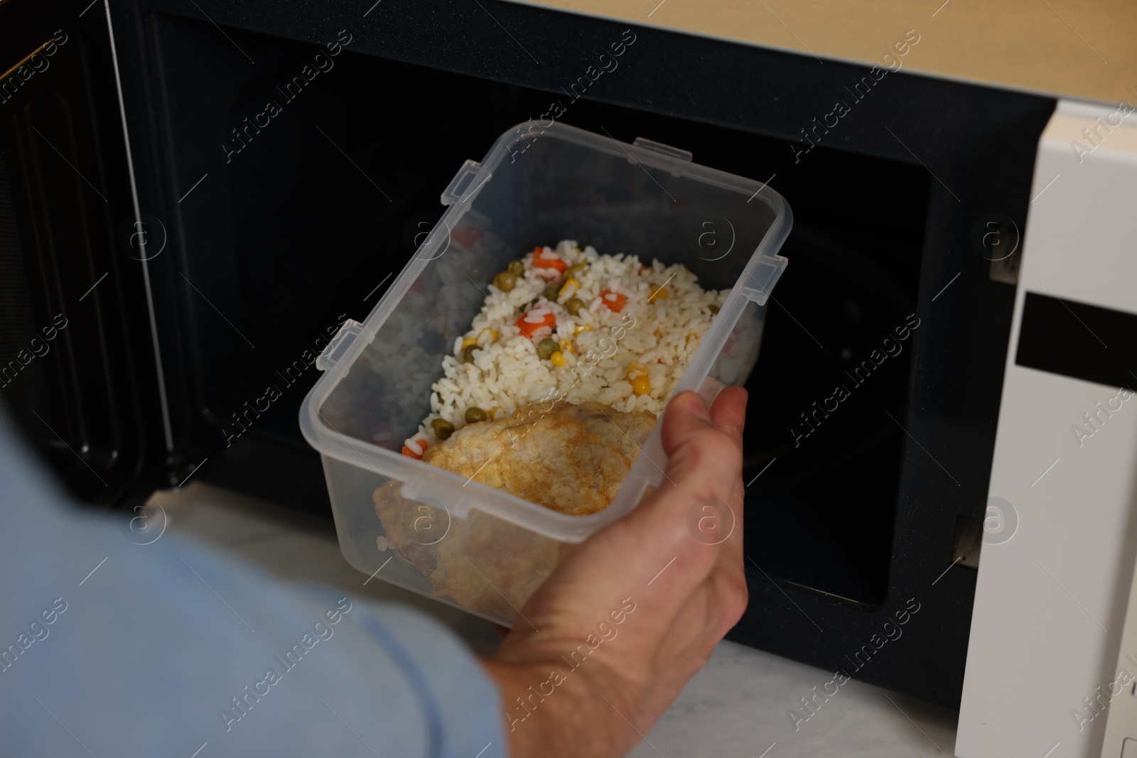 Photo of Man putting container with lunch into microwave in kitchen, closeup