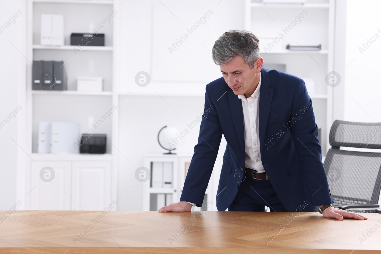 Photo of Man looking at something on desk in office. Space for text