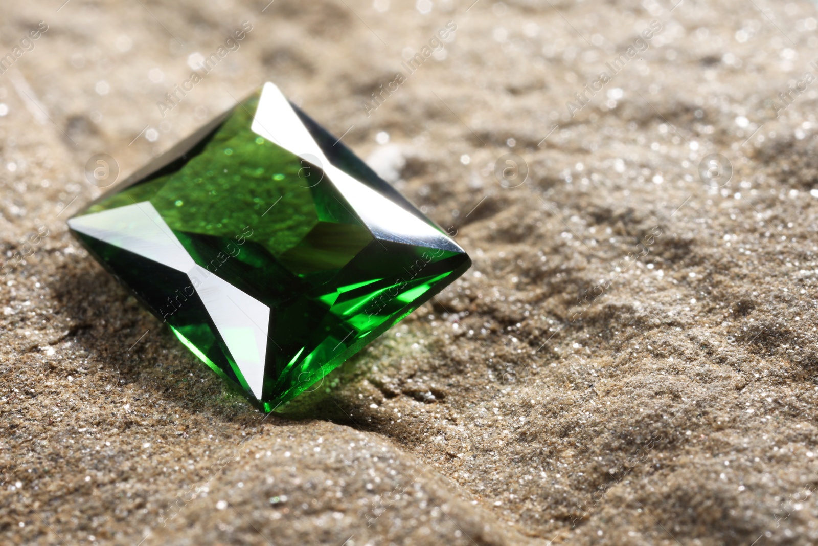 Photo of Beautiful shiny green gemstone on stone, closeup. Space for text