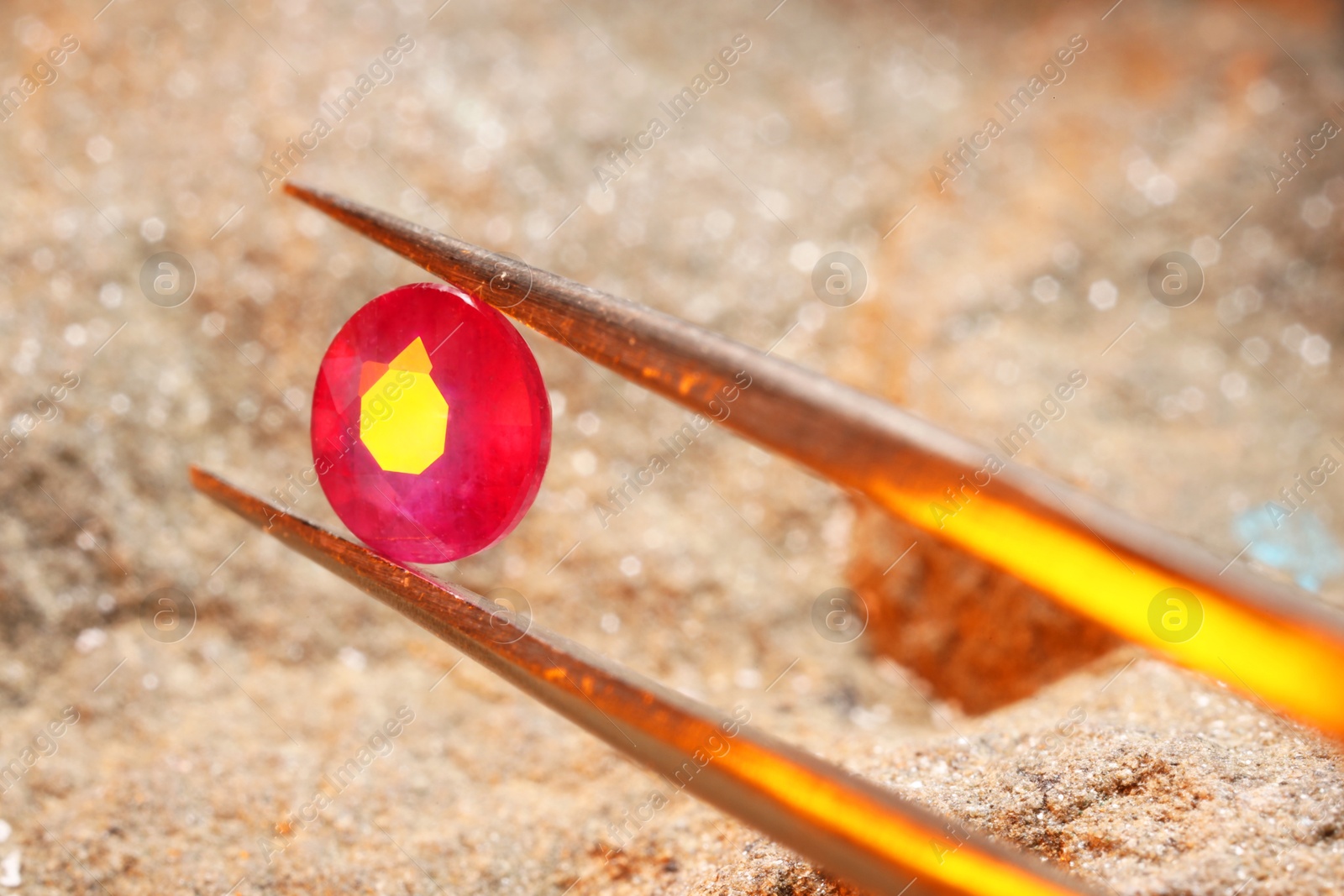 Photo of Tweezers with beautiful pink gemstone on stone, closeup