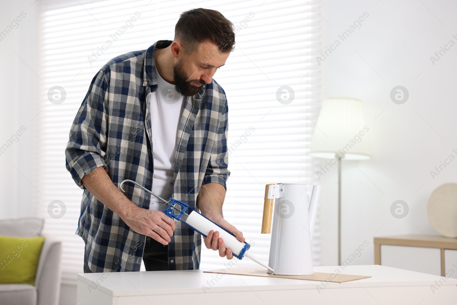 Photo of Man with caulking gun glueing watering can indoors