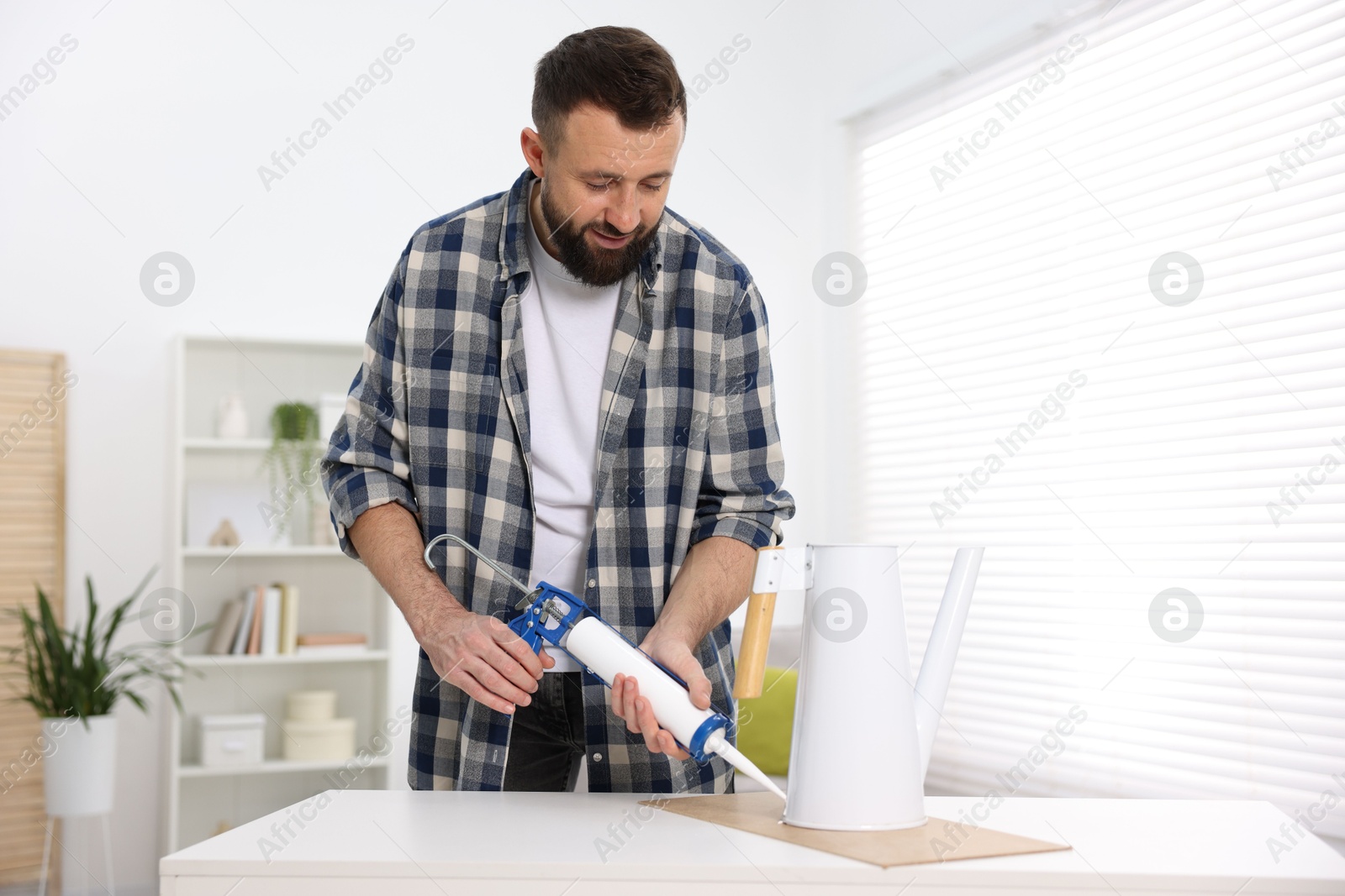 Photo of Man with caulking gun glueing watering can indoors