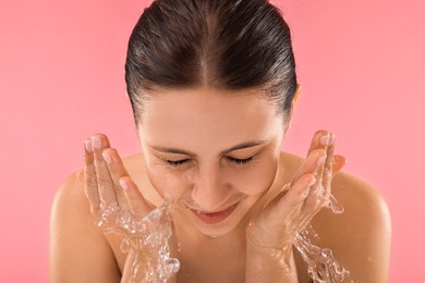 Attractive woman washing her face on pink background