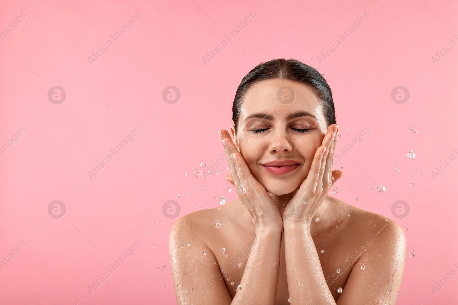 Photo of Attractive woman washing her face on pink background. Space for text