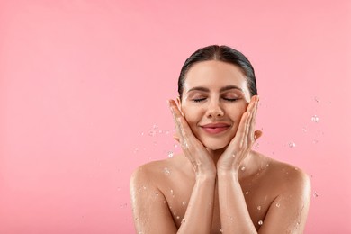 Photo of Attractive woman washing her face on pink background. Space for text