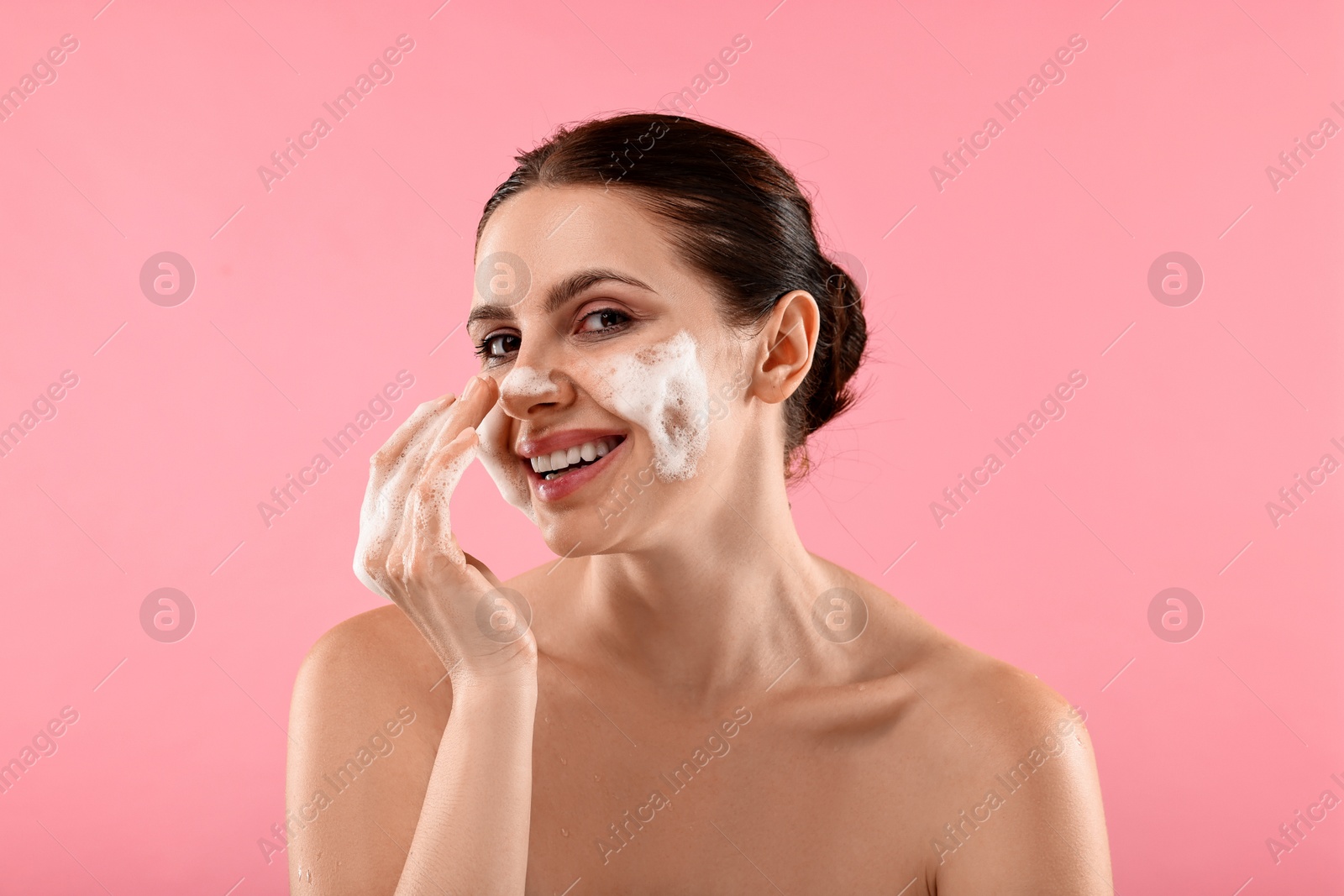 Photo of Smiling woman washing her face with cleansing foam on pink background