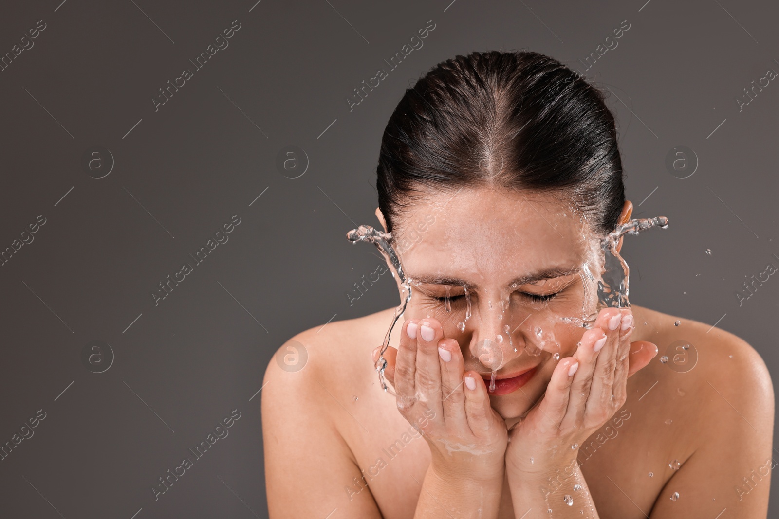 Photo of Woman washing her face on grey background, space for text