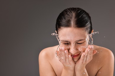 Woman washing her face on grey background, space for text