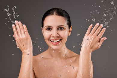 Smiling woman washing her face on grey background