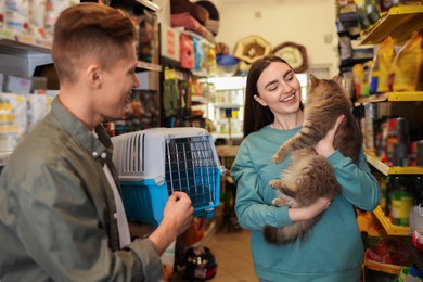 Photo of Couple choosing carrier for their cute cat in pet shop