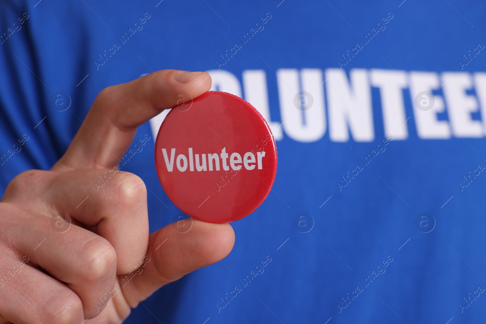 Photo of Man holding button badge with word Volunteer, closeup