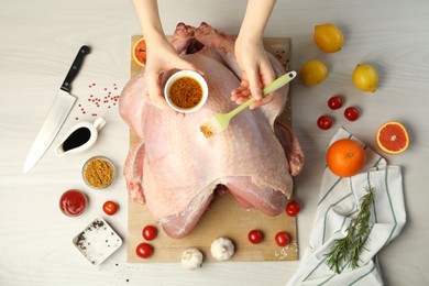 Photo of Woman applying marinade onto raw turkey at white wooden table, top view