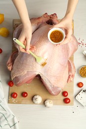 Photo of Woman applying marinade onto raw turkey at white wooden table, top view