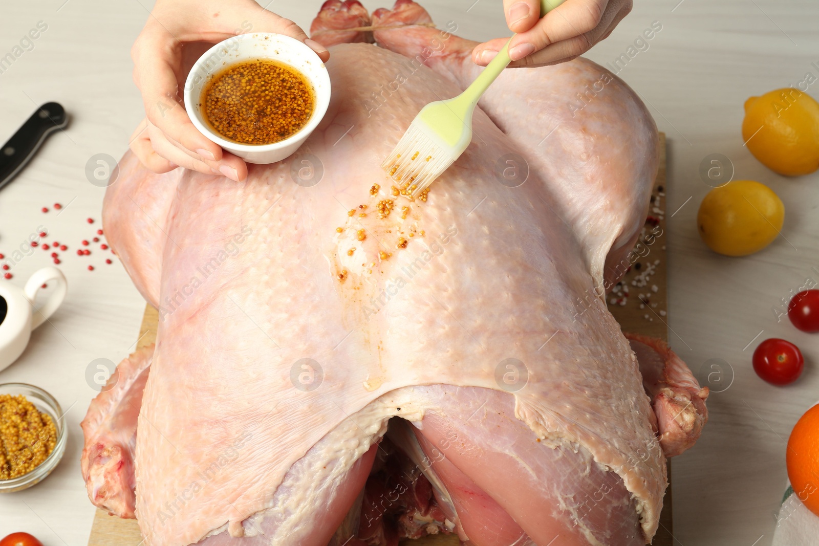 Photo of Woman applying marinade onto raw turkey at white wooden table, closeup