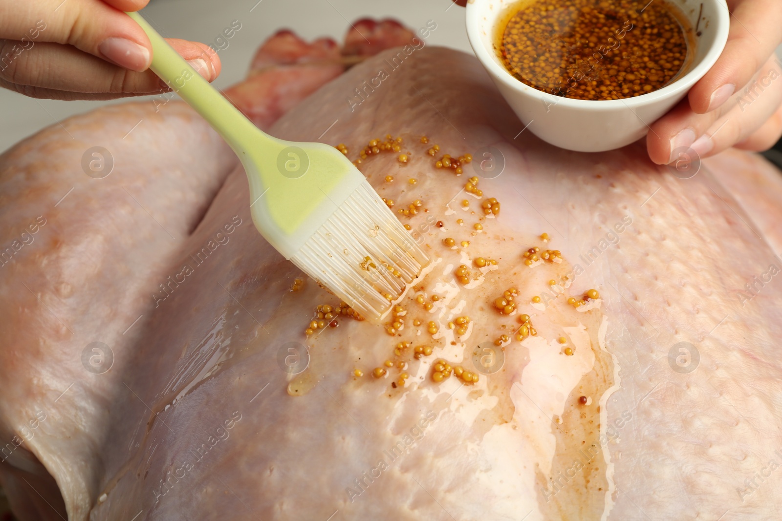 Photo of Woman applying marinade onto raw turkey at table, closeup