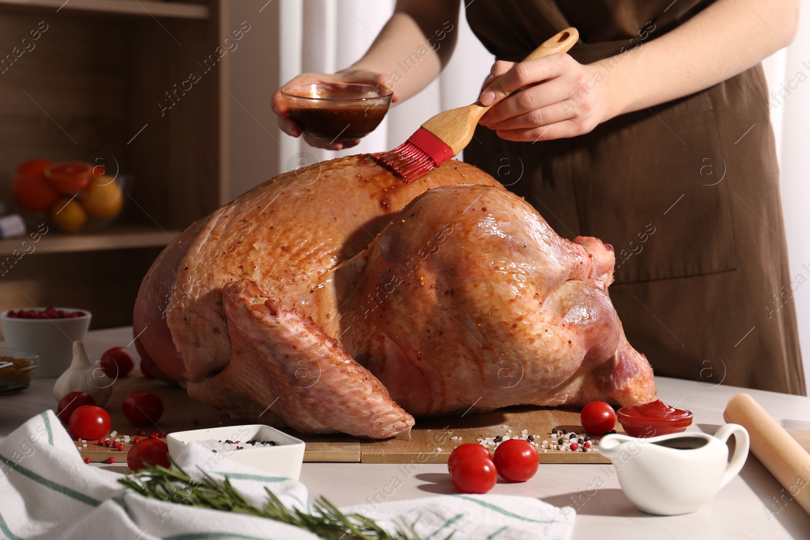 Photo of Woman applying marinade onto raw turkey at white wooden table, closeup