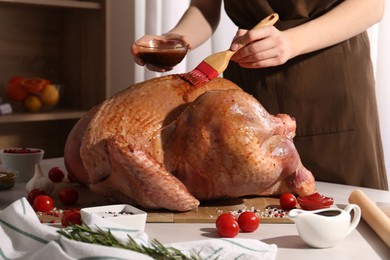 Photo of Woman applying marinade onto raw turkey at white wooden table, closeup