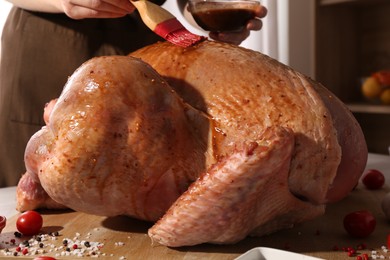 Photo of Woman applying marinade onto raw turkey at table, closeup