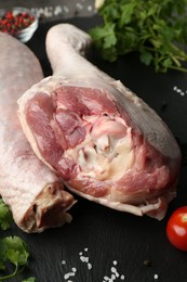 Photo of Raw turkey drumsticks and ingredients on black board, closeup