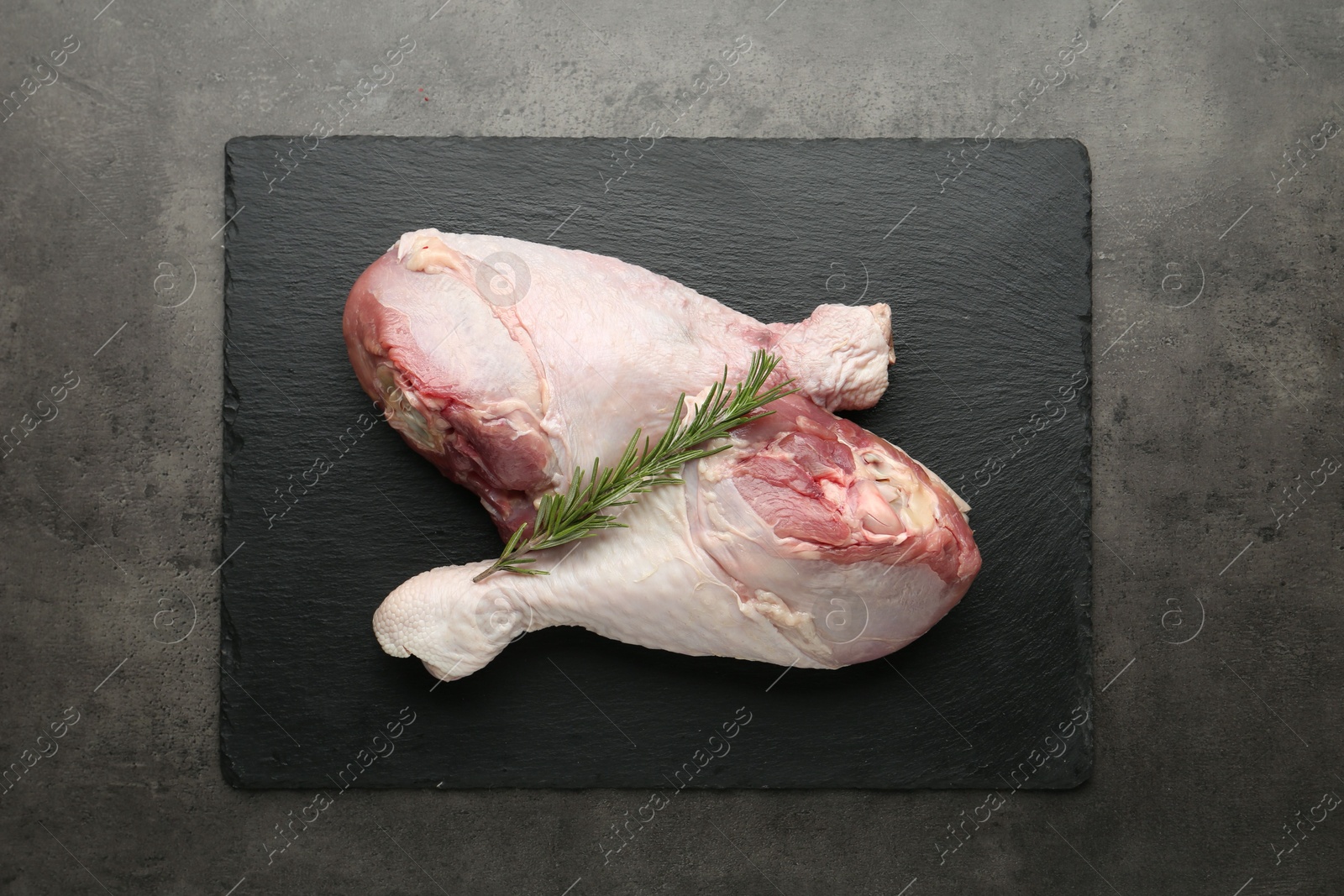 Photo of Raw turkey drumsticks and rosemary on grey table, top view