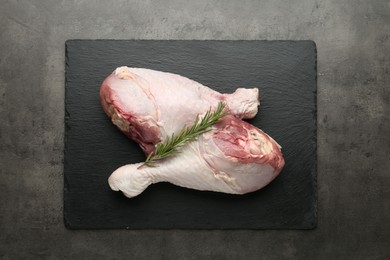 Photo of Raw turkey drumsticks and rosemary on grey table, top view