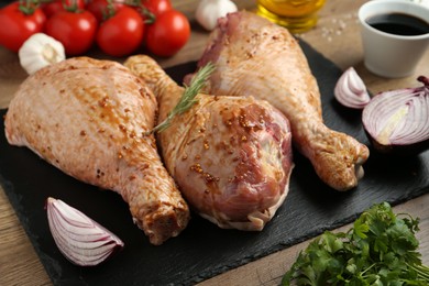 Photo of Raw marinated turkey drumsticks and products on wooden table, closeup